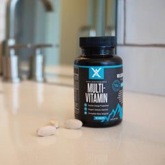 Wilderness Athlete High Performance Multivitamin bottle on a desk with active lifestyle gear.
