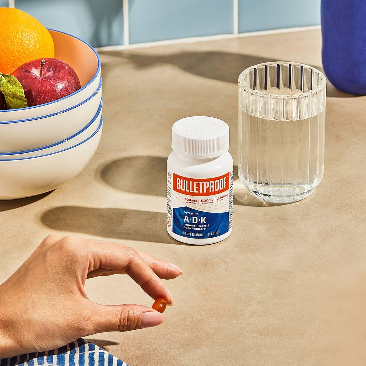 Bulletproof A-D-K softgels in hand suggesting a simple daily wellness ritual.